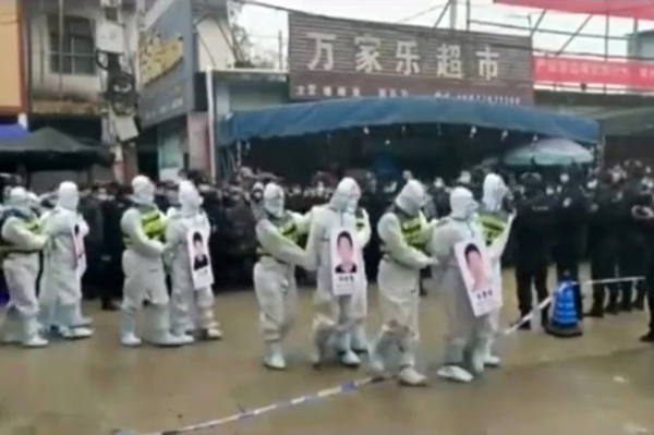 방호복을 입은 용의자 4명이 사진과 이름이 적힌 플래카드를 걸고 중국 광시(廣西)성 징시(靖西)시의 많은 군중 앞에서 행진했다. /트위터 캡처