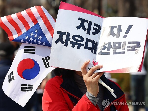 헌재의 윤석열 전 대통령 탄핵 인용이 발표된 지난 4일, 서울 용산 대통령실 인근에서 한 지지자가 피켓으로 얼굴을 가린채 길을 지나고 있다. /연합